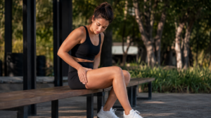 Dor na frente da coxa depois do treino: o que pode ser? Mulher após o treino tocando a parte da frente da coxa devido a desconforto muscular.
